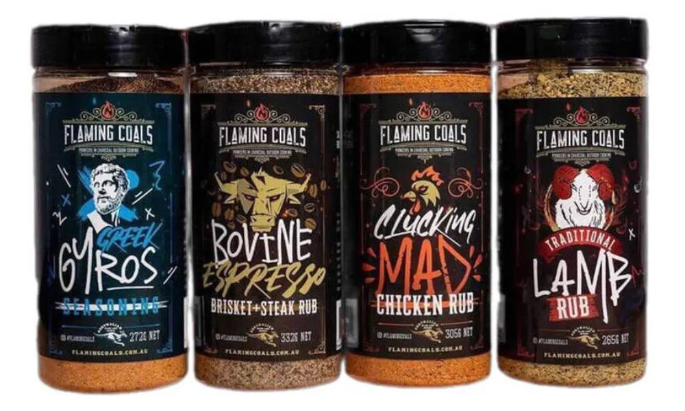 The Flaming Coals Ultimate Rub Rack featuring four BBQ seasoning blends in a gift pack — Clucking Mad Chicken Rub, Bovine Espresso Brisket & Steak Rub, Greek Lamb Rub, and Porkinator Pork Rub. Each bottle is designed with bold artwork and tailored for chicken, beef, lamb, and pork. The Flaming Coals Ultimate Rub Rack featuring four BBQ seasoning blends in a gift pack — Clucking Mad Chicken Rub, Bovine Espresso Brisket & Steak Rub, Greek Lamb Rub. Each bottle is designed with bold artwork and tailored for chicken, beef and lamb
