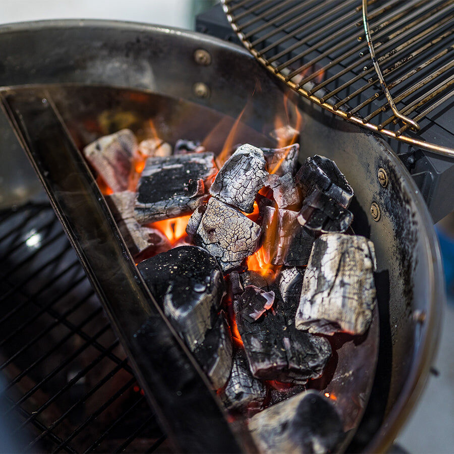 Close-up of glowing lump charcoal burning in a charcoal BBQ, with flames and white ash on the surface of the irregularly shaped natural wood pieces.