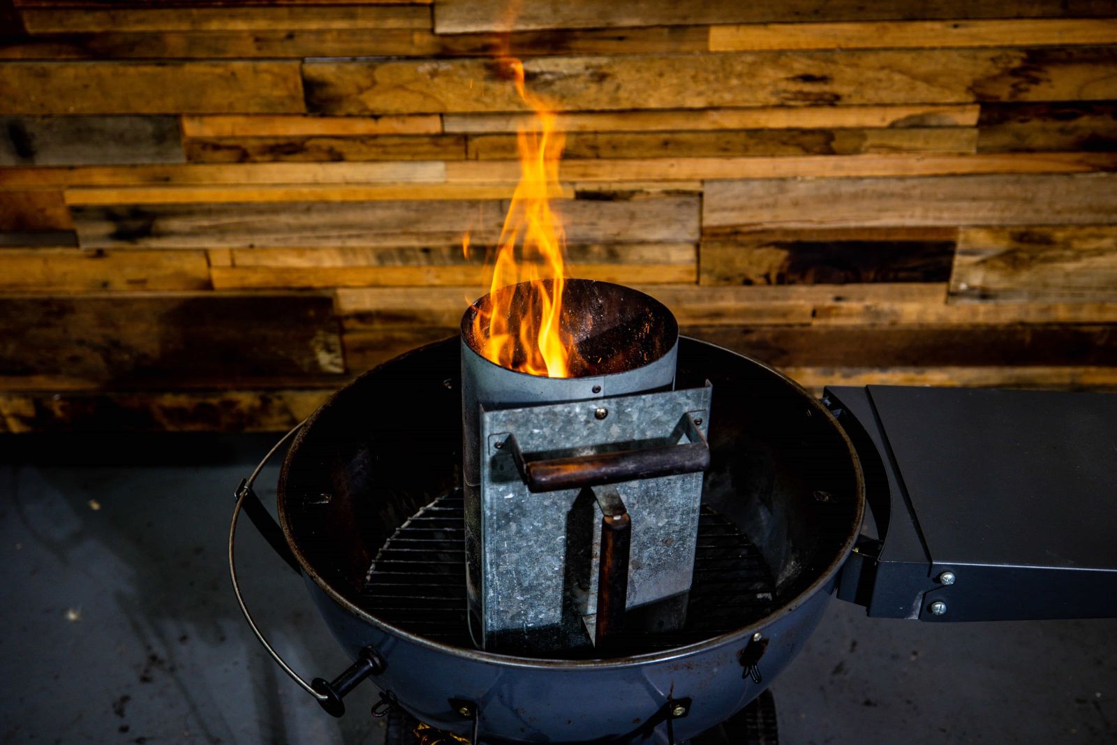 Charcoal chimney starter filled with burning coals producing tall orange flames, placed on top of a charcoal BBQ grill. Charcoal chimney starter filled with burning coals producing tall orange flames, placed on top of a charcoal BBQ grill.