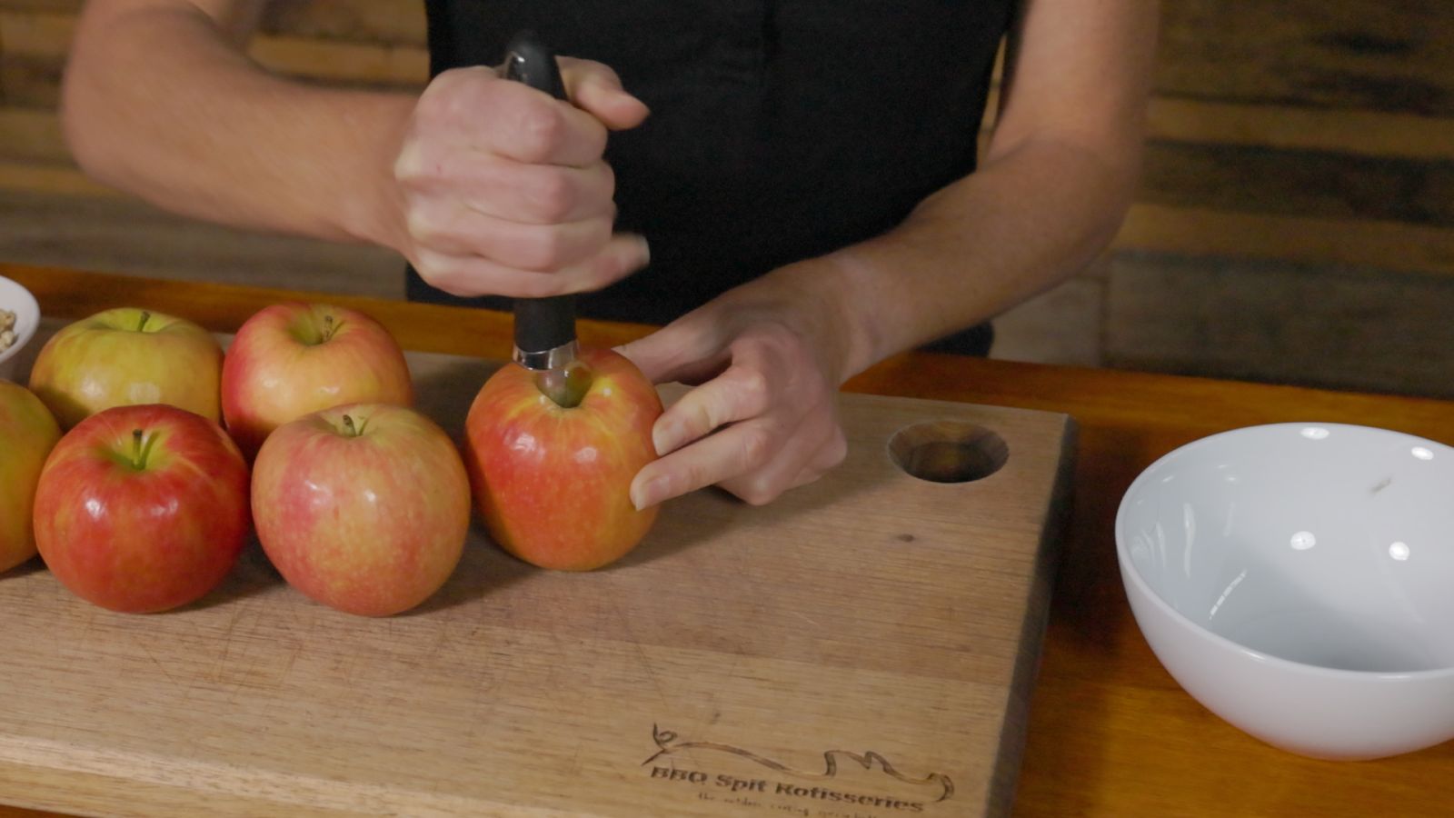 Person using a corer to remove the centre of fresh apples on a wooden chopping board.