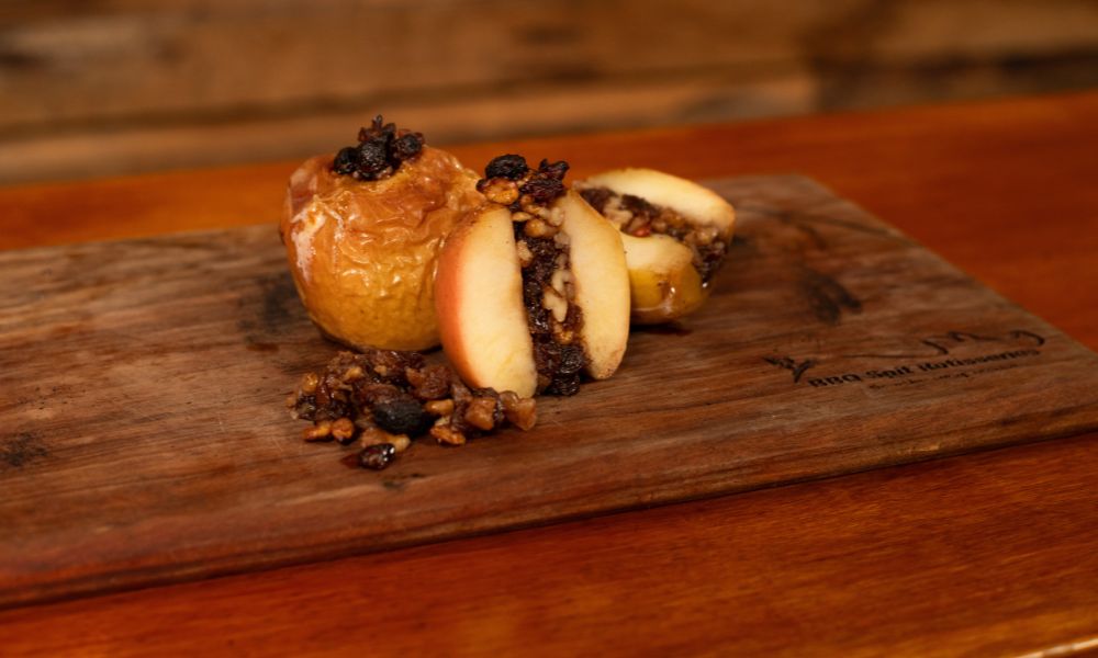 Baked apple stuffed with walnuts, raisins, and honey, sliced open to reveal the warm spiced filling on a wooden serving board.