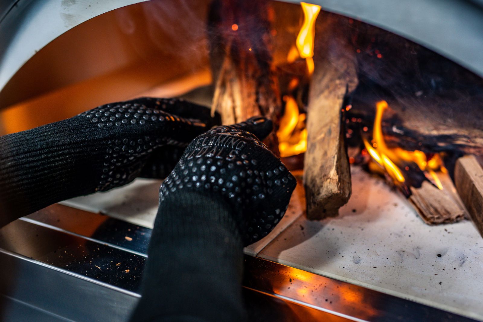 This image shows the long heat proof gloves managing wood in the pizza oven.