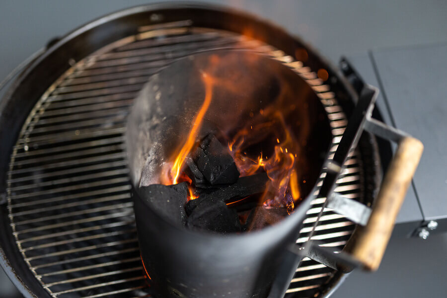 Charcoal chimney starter filled with burning coals inside a BBQ grill, showing flames and glowing embers ready for cooking. Charcoal chimney starter filled with burning coals inside a BBQ grill, showing flames and glowing embers ready for cooking.