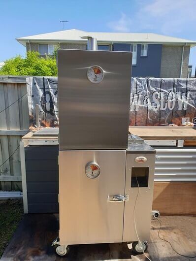 Extra large stainless steel gravity feed smoker situated in an outdoor BBQ area