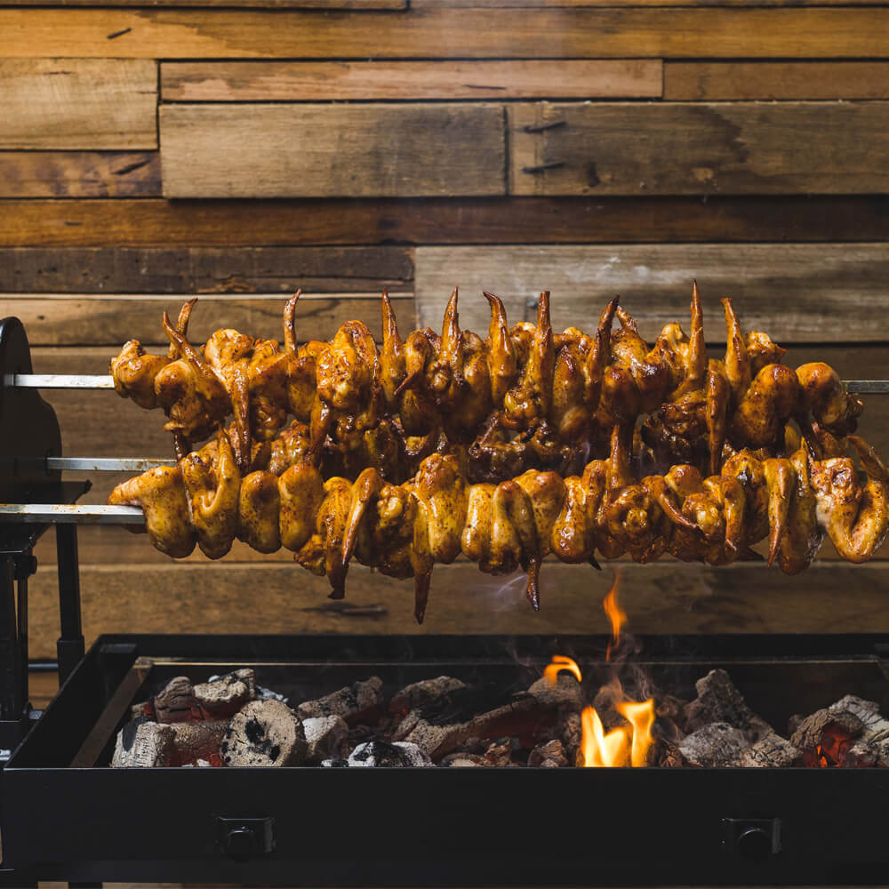 olden chicken wings cooking on a double skewer Cyprus spit over glowing charcoal embers, creating perfectly crisp, flame-kissed skin.