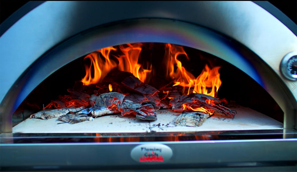 Wood fired pizza oven with burning logs and glowing embers creating intense heat for cooking.