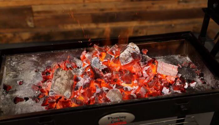 Glowing lump charcoal burning in a Flaming Coals Cyprus Spit, with red-hot coals and ash radiating heat.