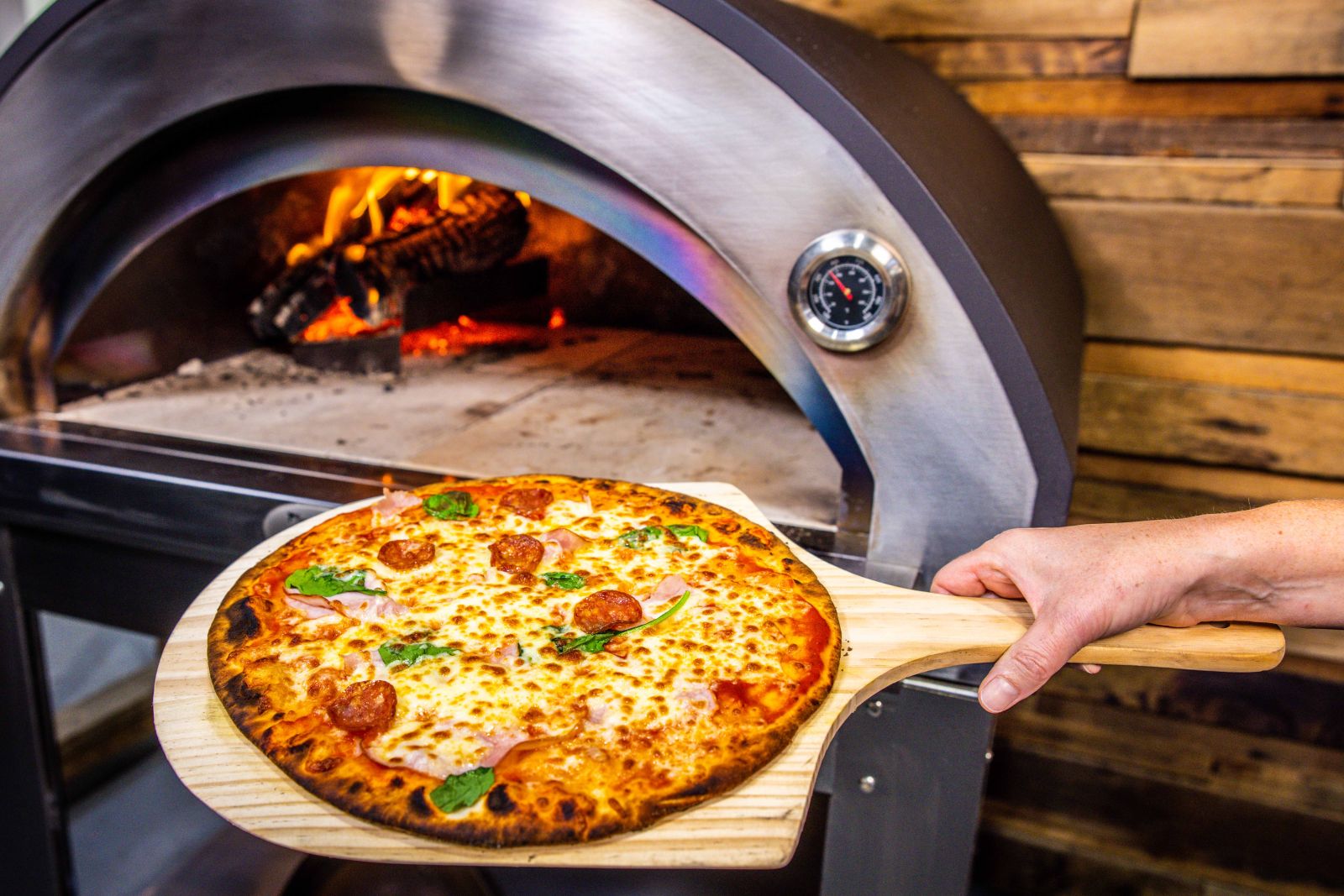 Freshly cooked pepperoni pizza on a wooden paddle taken out of a premium Flaming Coals wood fired pizza oven.