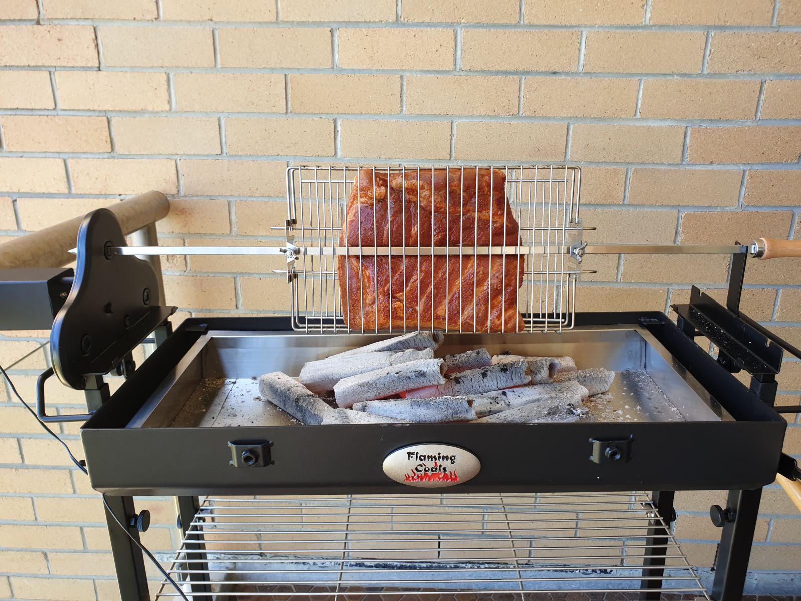 Pork belly cooking in a large multi-use rotisserie basket over hot charcoal on a Flaming Coals Cyprus Spit.