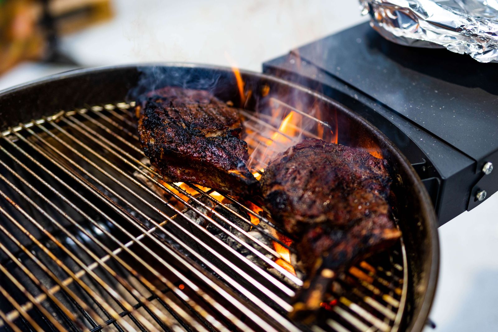 Ribeye steaks grilling over charcoal kettle BBQ