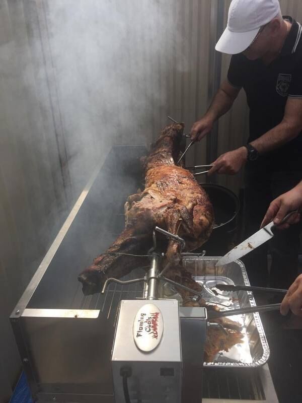 Whole lamb roasting on a Flaming Coals Spartan Spit Roaster with stainless steel motor and carving in progress.