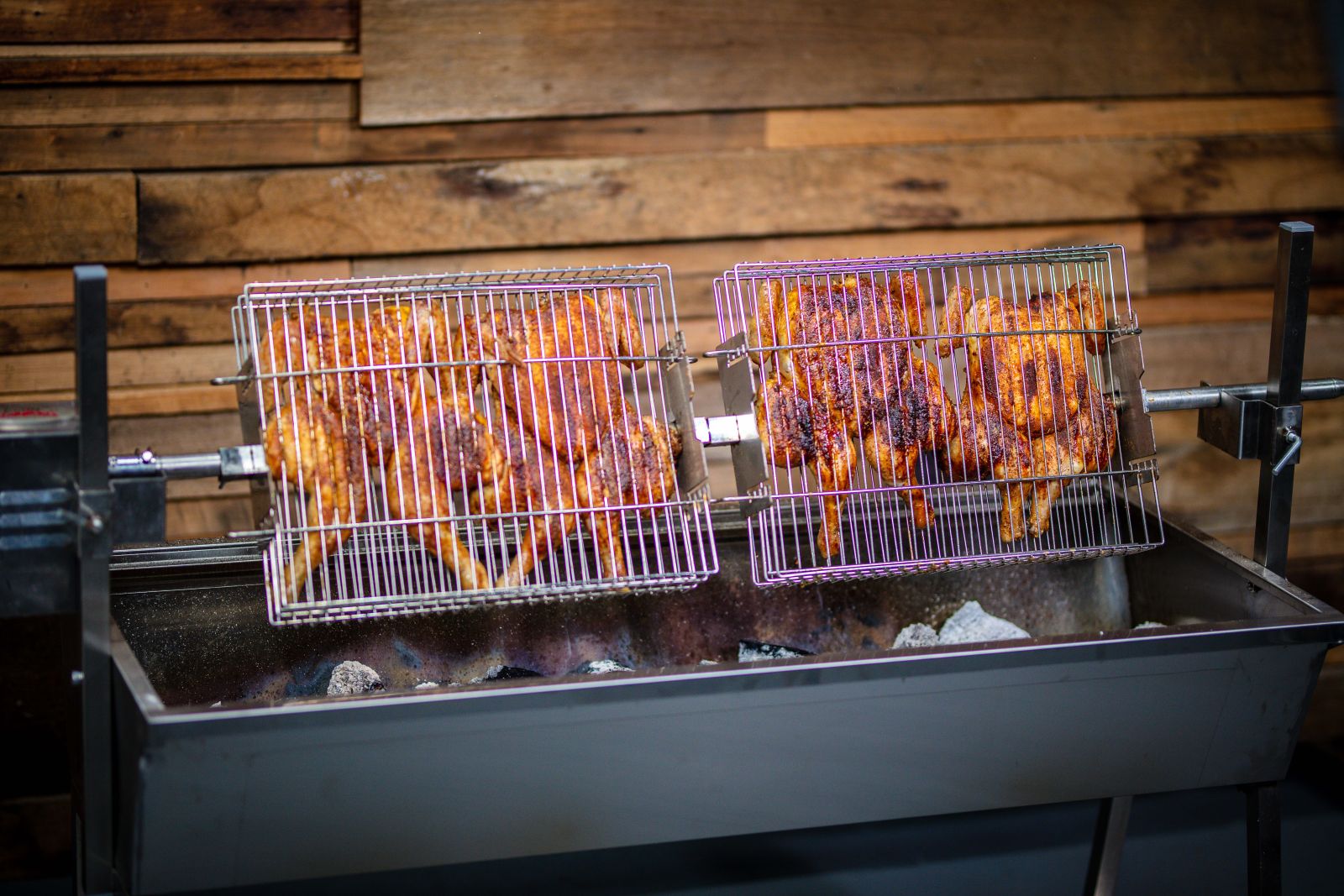 Chickens roasting over charcoal in stainless steel baskets on a Flaming Coals Master Spit Rotisserie.