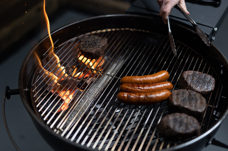Steaks and sausages grilling with indirect heat on kettle BBQ