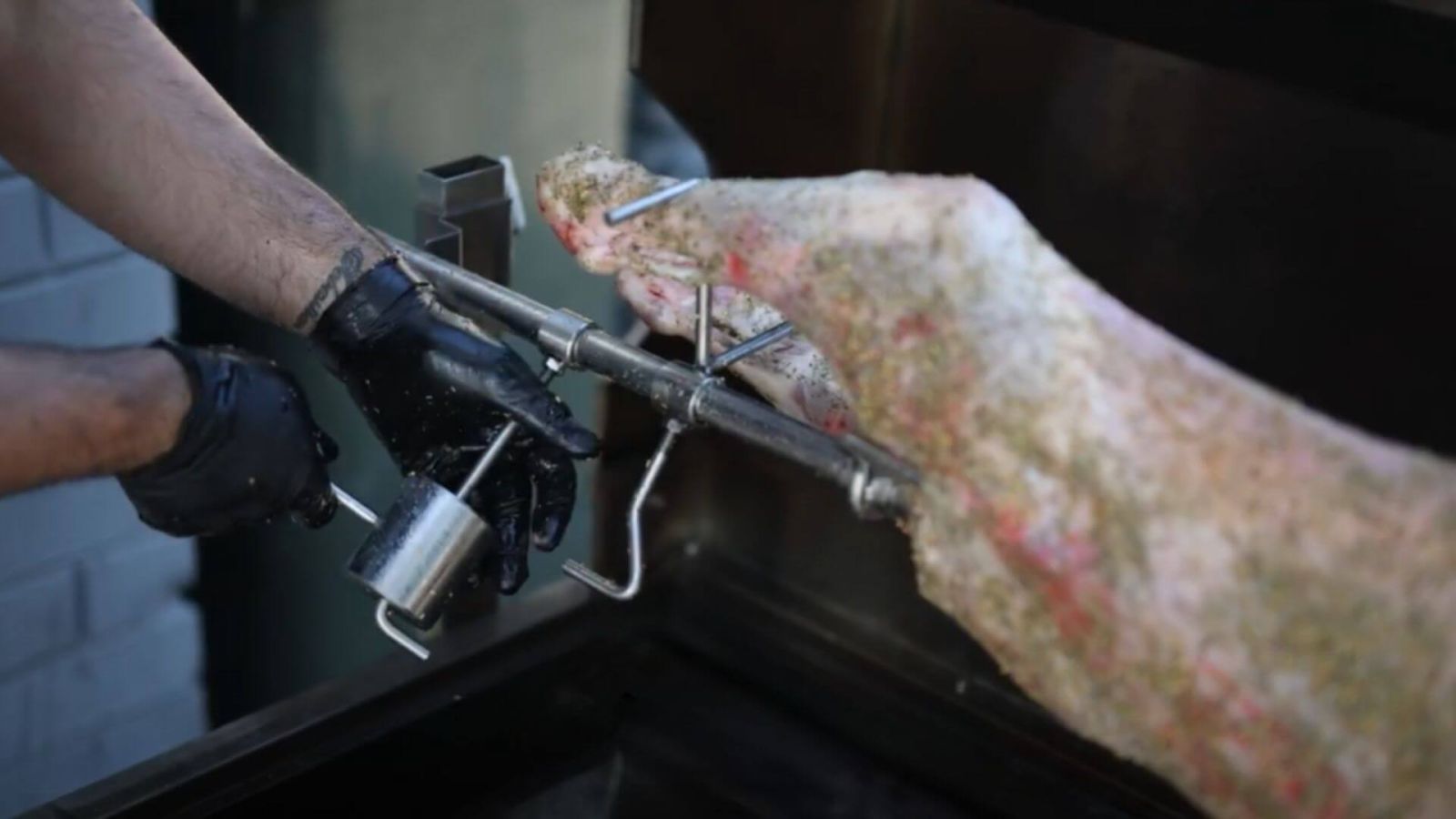 Attaching a counterbalance weight to a rotisserie shaft to reduce motor strain while cooking a whole lamb.