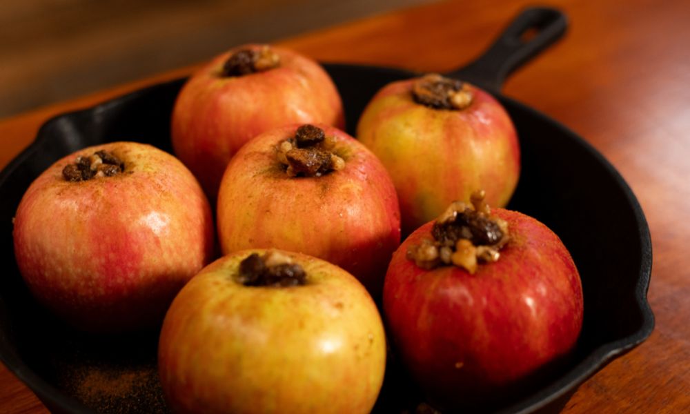 Fresh apples stuffed with a mixture of honey, walnuts, and raisins placed in a cast iron skillet, ready for baking.