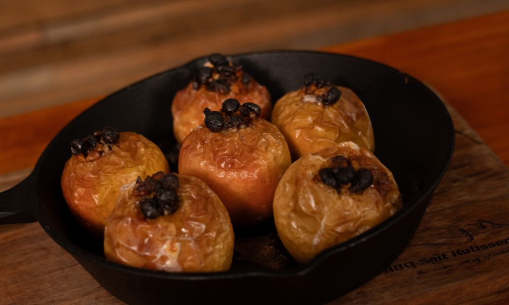 Baked apples in a cast iron pan cooked in a wood fired pizza oven, golden brown with caramelised tops.
