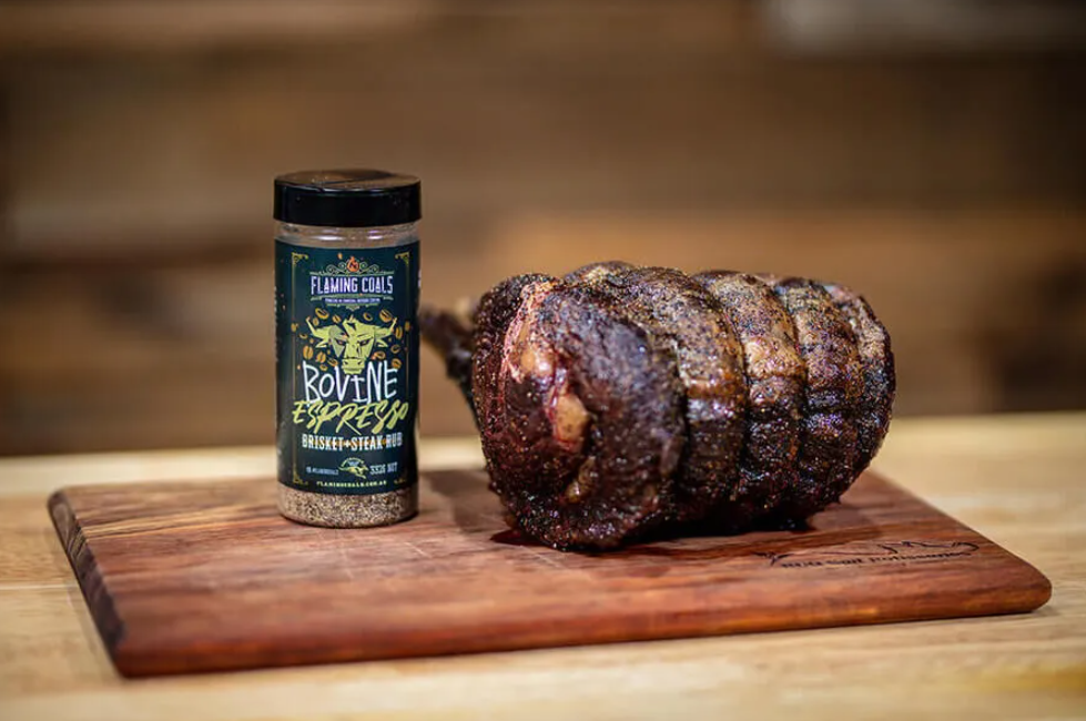 Beef roast on wooden board beside Bovine Espresso brisket and steak BBQ rub seasoning jar.