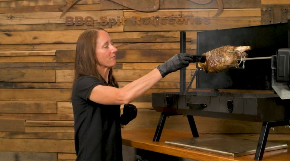 Leg of lamb cooking on a mini spit roaster indoors with motor turning over charcoal heat.