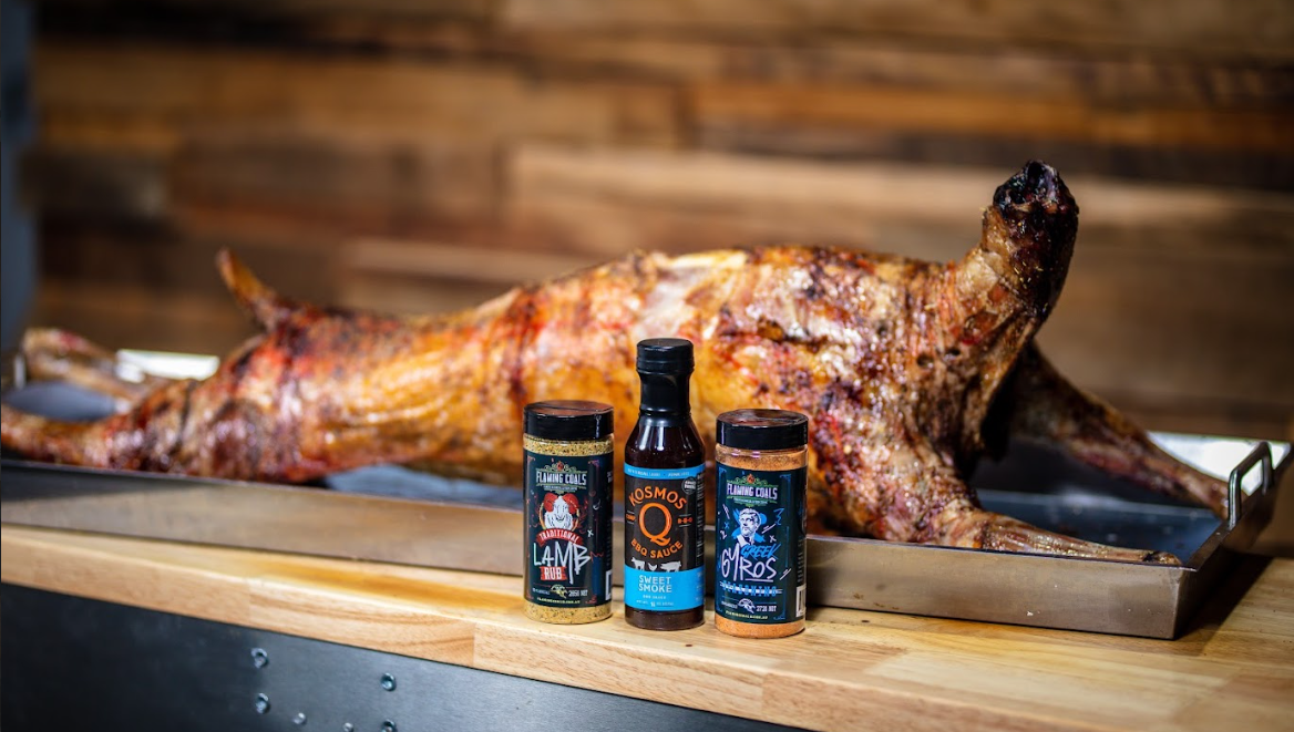 Cooked whole lamb on tray with BBQ rubs and sauce bottles displayed in front.
