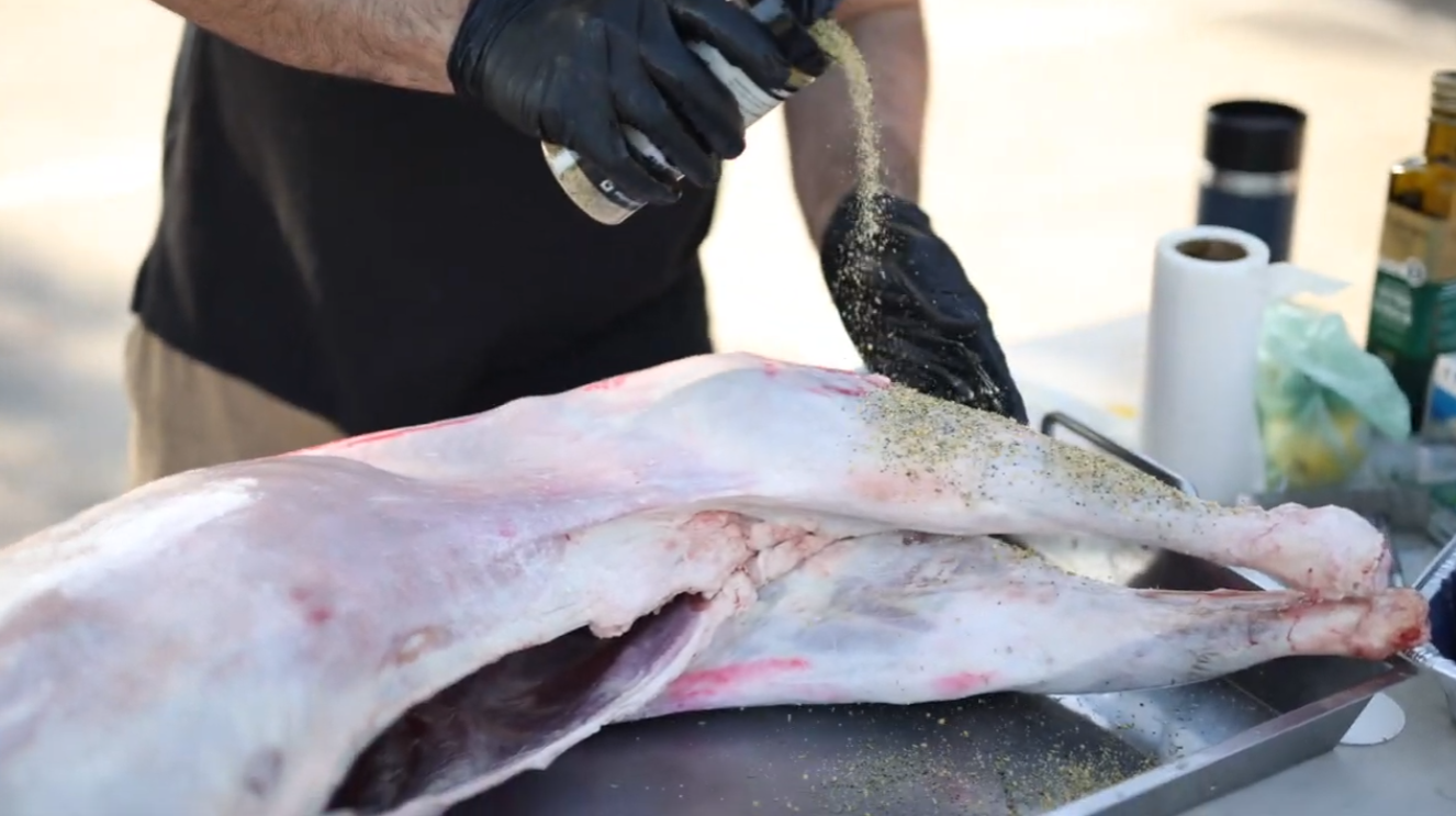 Whole lamb being seasoned with Flaming Coals Lamb Rub before cooking on a spit.