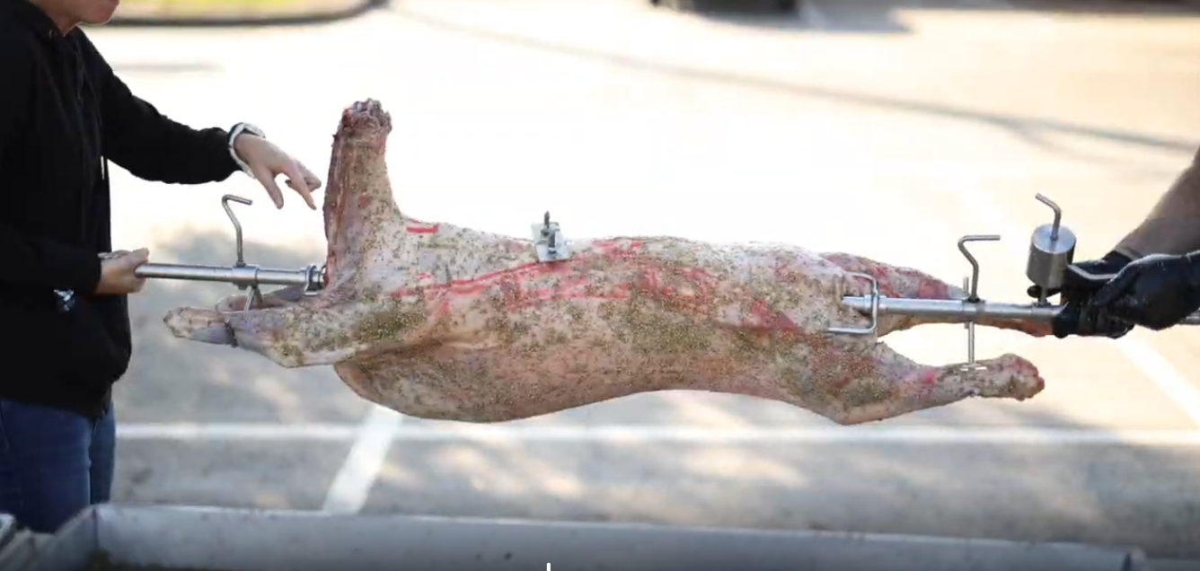 Seasoned whole lamb secured on a spit skewer, ready for rotisserie cooking.