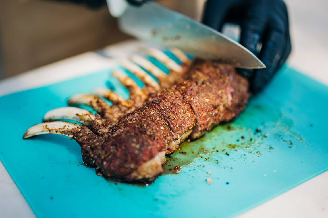 Slicing cooked lamb cutlets with herb seasoning on a cutting board